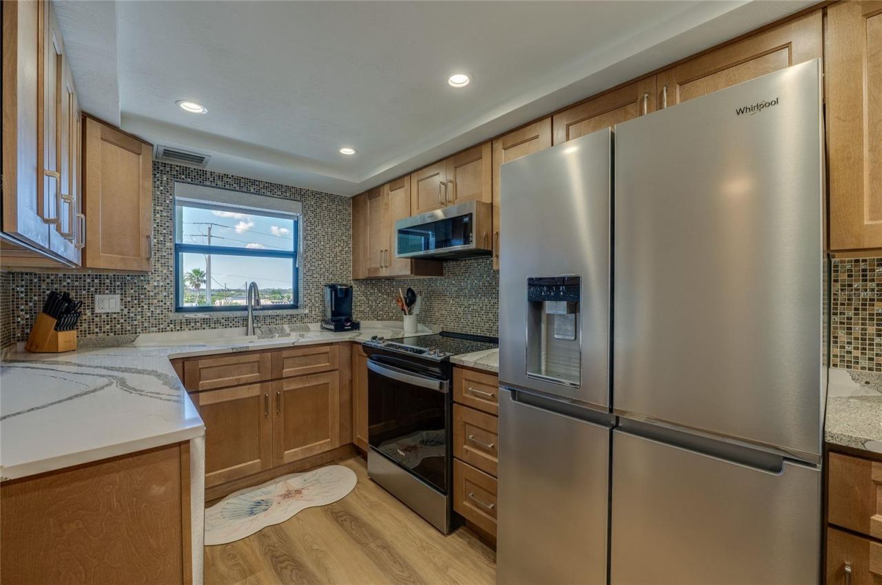 Photo 5 of 20: Updated kitchen featuring Cambria countertops, beautiful wood cabinetry, mosaic tile backsplash, and stainless steel appliances, all enhanced by recessed lighting and natural light from the window.