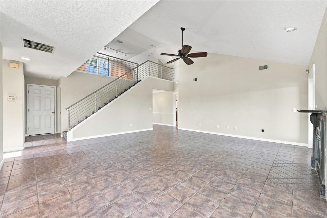 Photo 11 of 20: Living area — Open living space with tile flooring, staircase with cable railing to the loft, and natural light from the front entry doors.