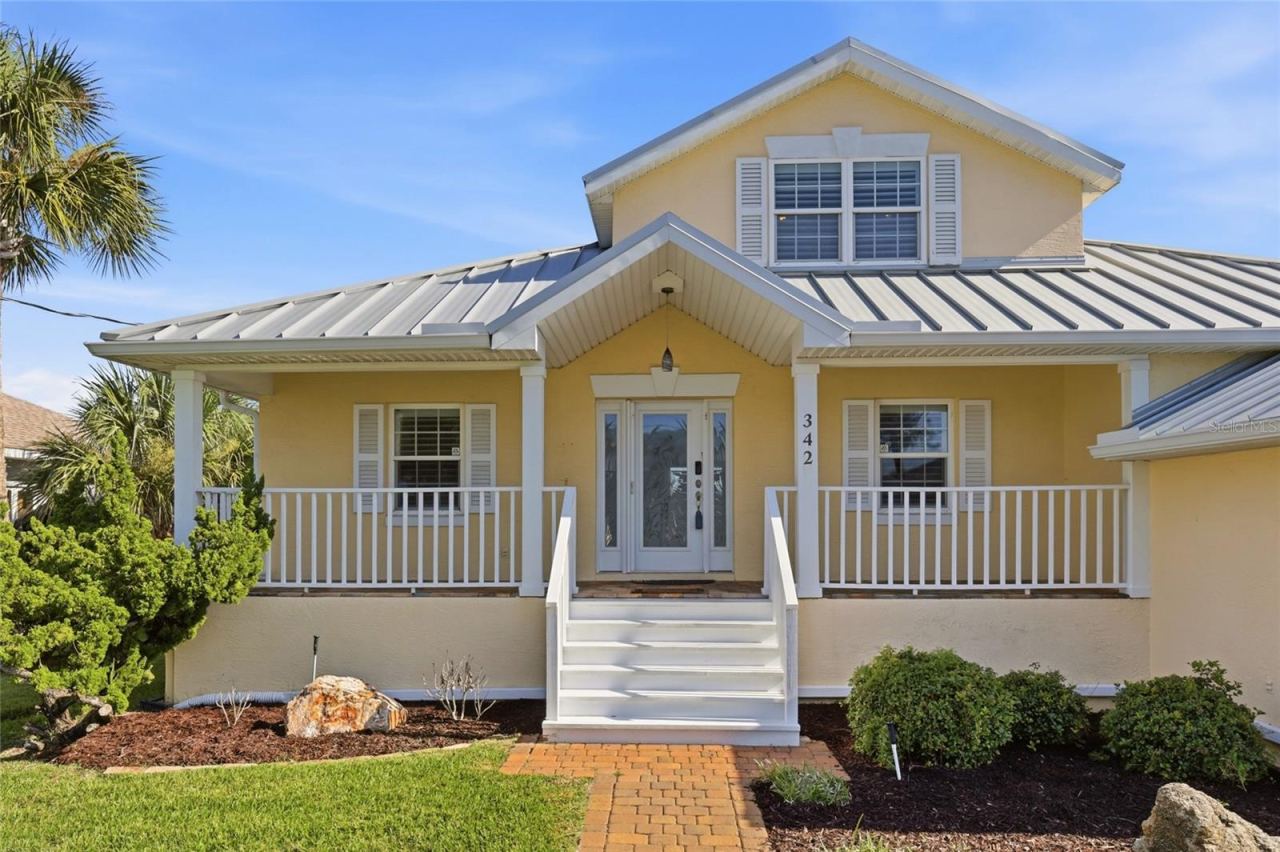 Photo 2 of 20: Front exterior — Front elevation with standing-seam metal roof, covered porch, painted railings, and paver walkway leading to the entry.