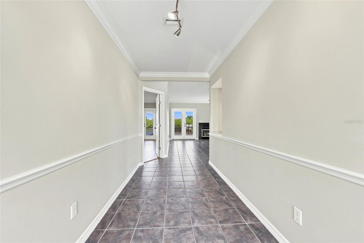 Photo 8 of 20: Interior hallway — Tiled hallway with crown molding and chair rail leading toward the living area, with French doors opening to a water-view balcony visible ahead.