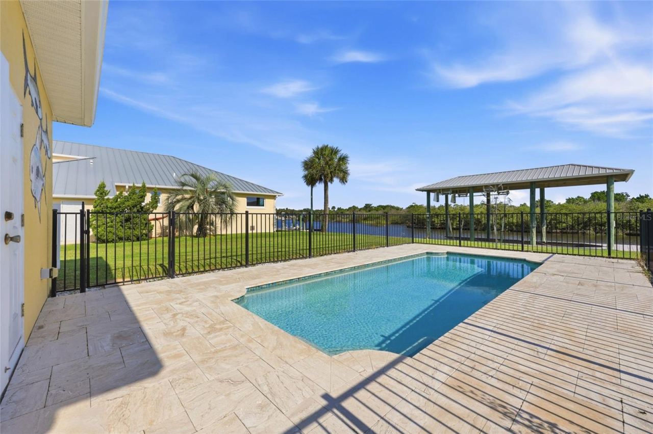 Photo 5 of 20: Pool area — Fenced backyard pool with paver deck, canal views, and a covered dock structure visible beyond the fence line.