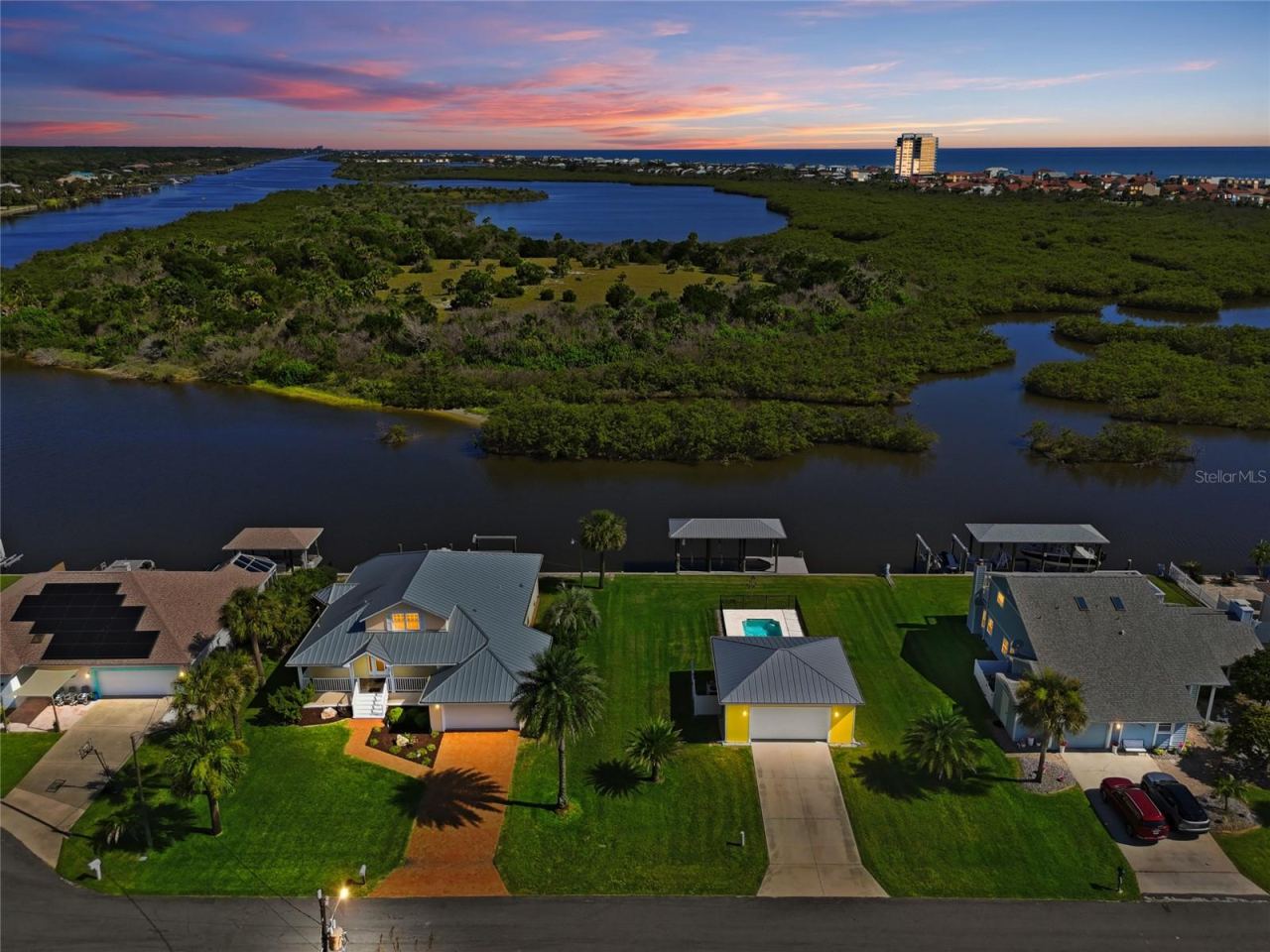 Photo 4 of 20: Aerial view (dusk) — Twilight aerial view of the canal-front home highlighting the dock with two covered boat lifts, backyard pool, and unobstructed water access to the Intracoastal Waterway.