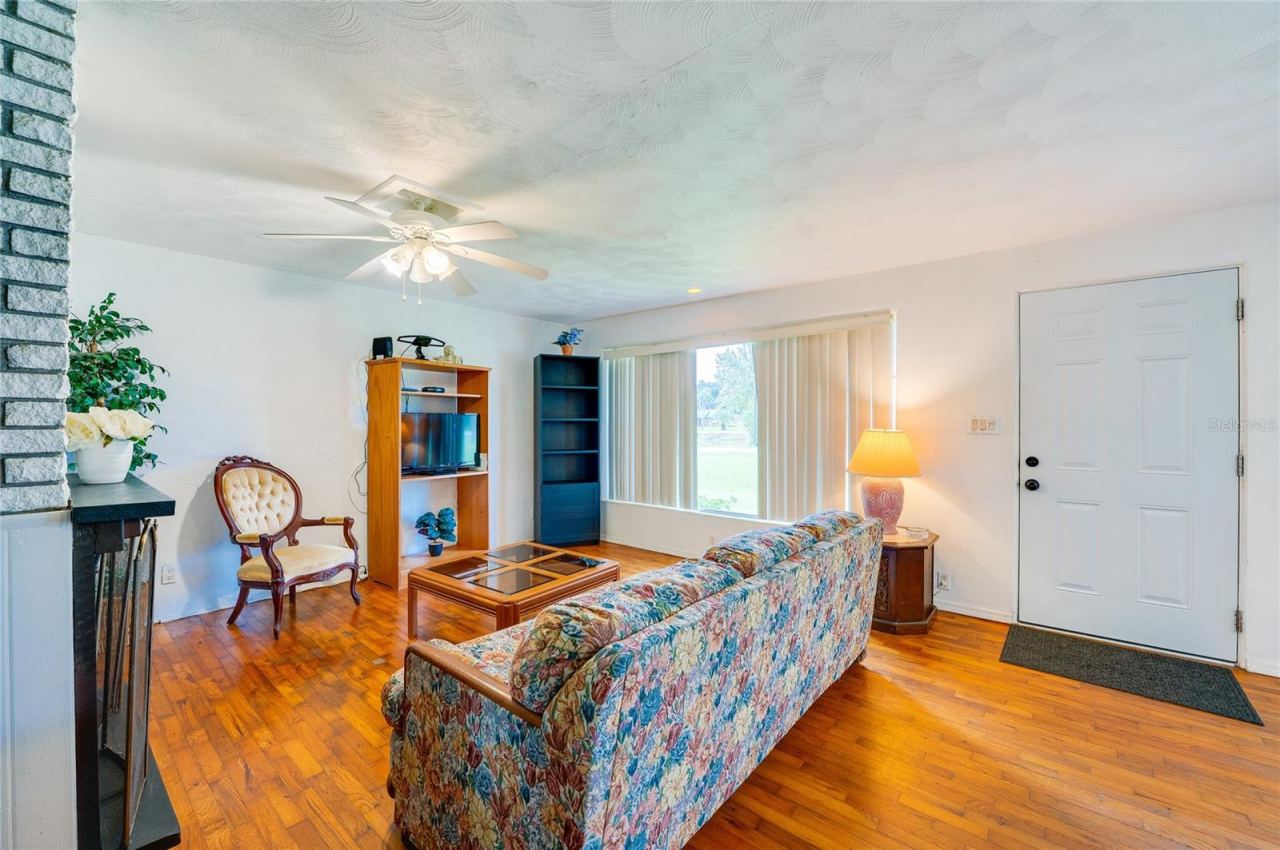Photo 7 of 20: Bright entryway and living zone showcasing gleaming hardwood floors, and a classic front door. Generous windows allow daylight to fill the open interior layout.