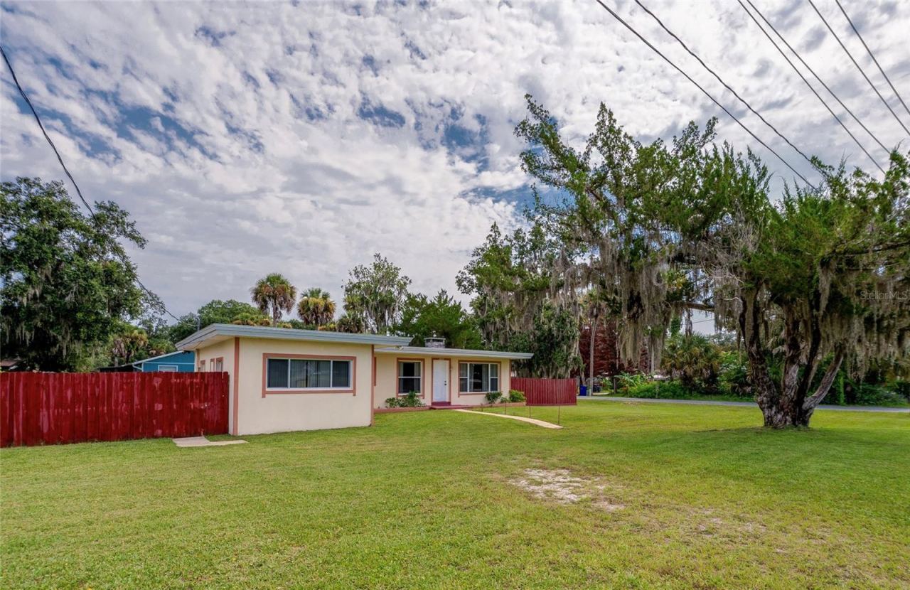Photo 1 of 20: Front view of the home highlighting a paved walkway, vibrant lawn, red fencing, and mature trees.