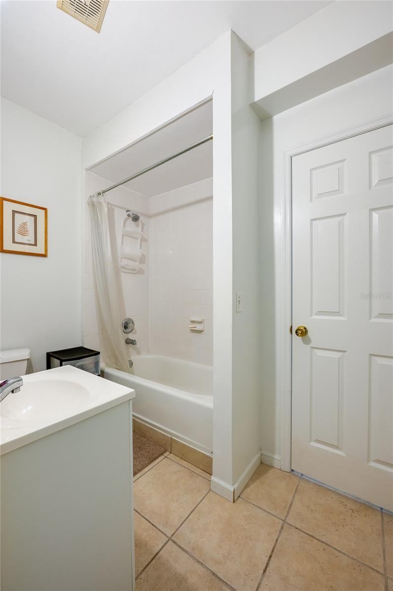 Photo 17 of 20: Clean bathroom area featuring a vanity sink, tiled floor, and a full bathtub with an overhead shower and curtain enclosure.