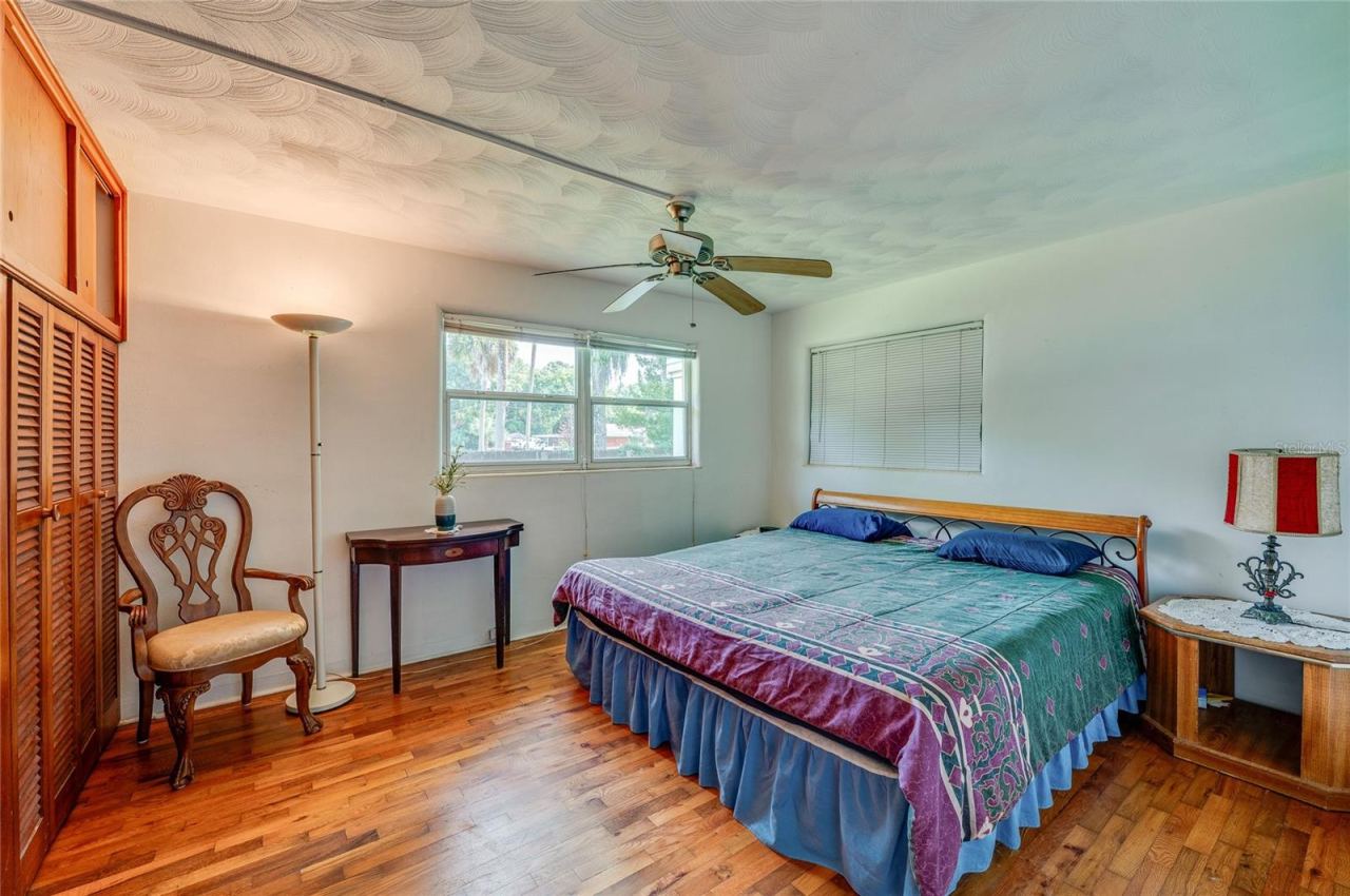 Photo 18 of 20: Spacious bedroom boasting rich hardwood floors, textured ceilings, a central ceiling fan, and extensive floor-to-ceiling built-in closets. Double windows invite soft natural light into the room.