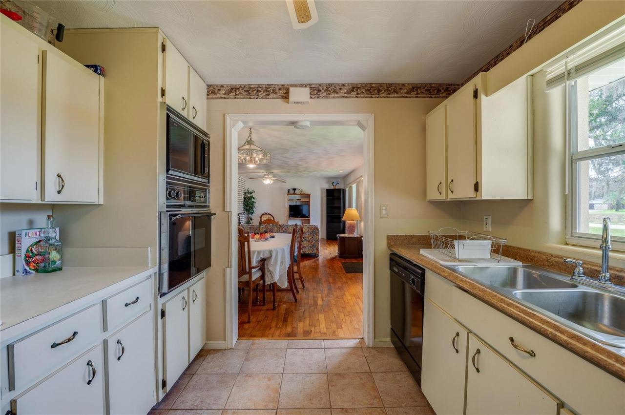 Photo 11 of 20: Centrally located kitchen framed by wall oven and ample cabinet storage, looking through an open doorway into the main living space.