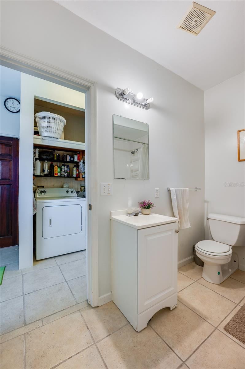 Photo 16 of 20: Bright bathroom layout showcasing a white pedestal-style vanity, toilet, tiled flooring, and a direct view into the adjoining laundry room.