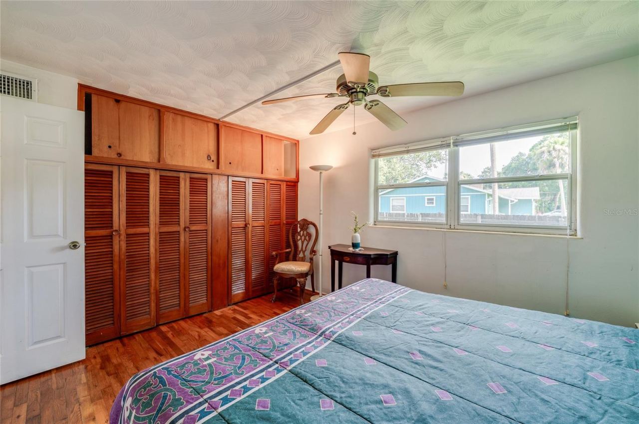 Photo 19 of 20: Light-filled bedroom featuring built-in closet storage, rich wood floors, and an overhead ceiling fan. Wide windows deliver pleasant outdoor views and plenty of daytime illumination.