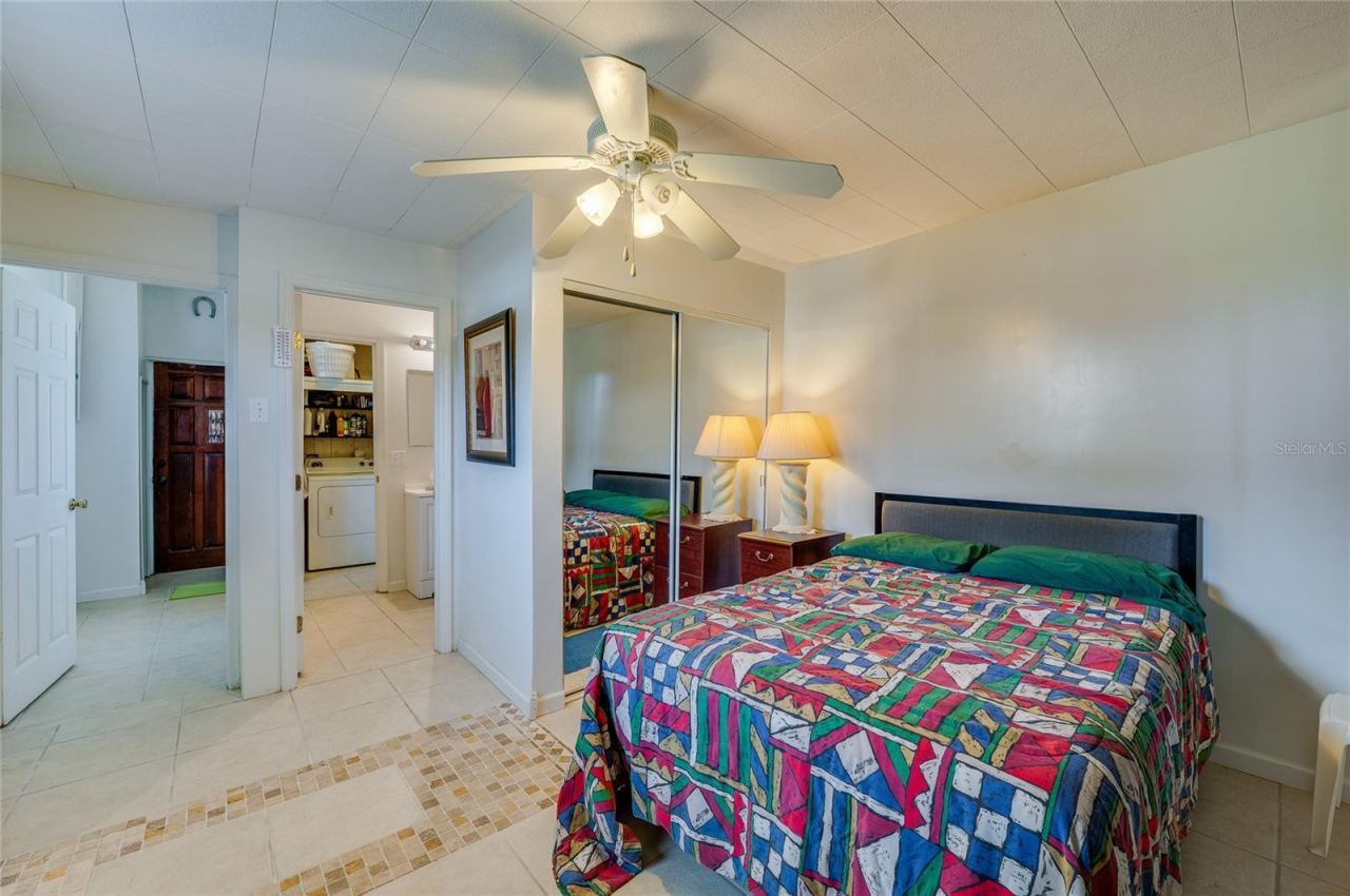 Photo 15 of 20: Tiled bedroom layout showcasing mirrored closet doors, a ceiling fan, and open doorway access toward the bathroom and utility spaces.