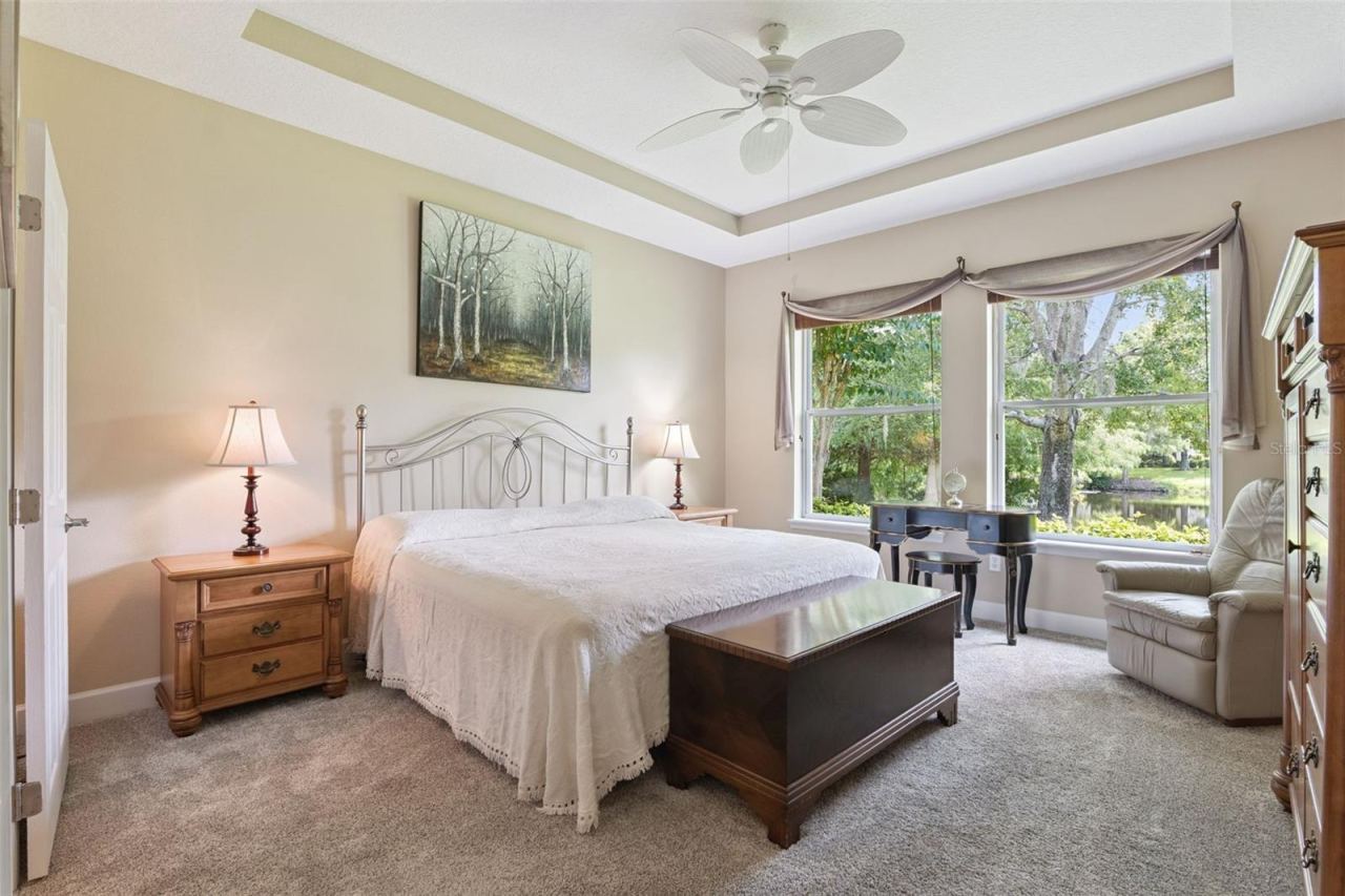 Photo 16 of 20: 13'6" x 14'9" Primary Bedroom w/ a tray ceiling, ceiling fan & a Pond view