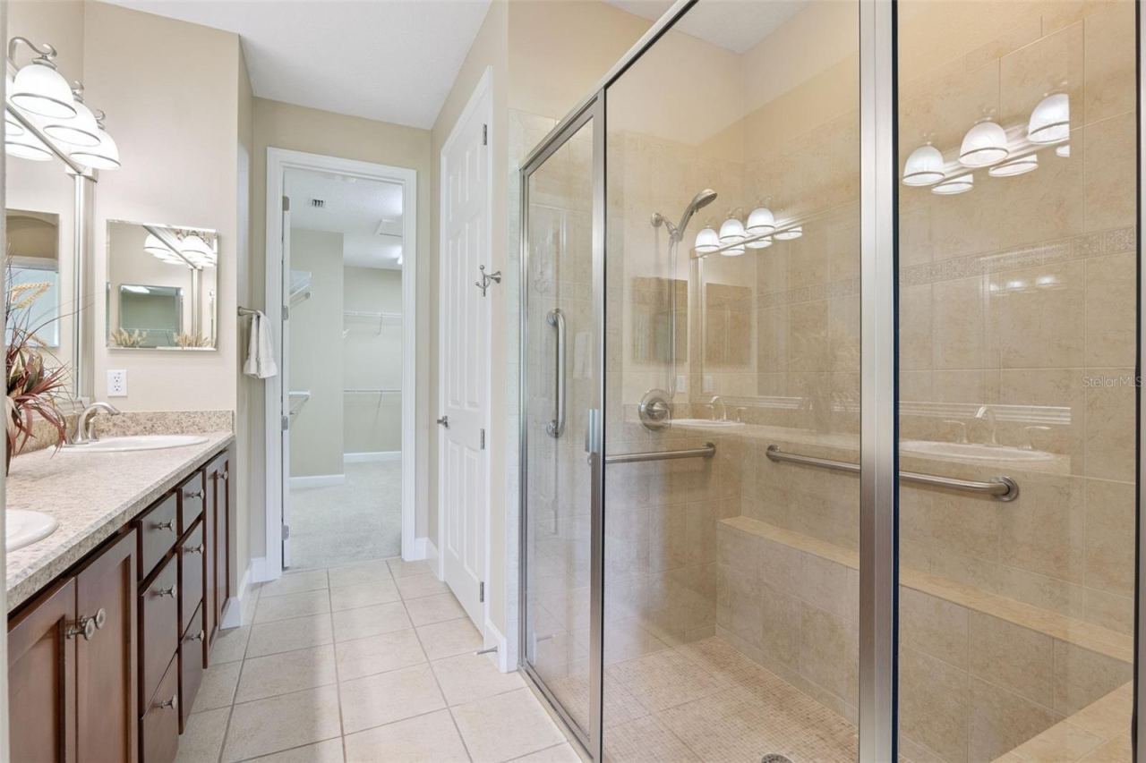 Photo 19 of 20: Primary Bathroom w/ a glass enclosed walk-in shower, bench seat, grab bars & a vanity w/ dual sinks