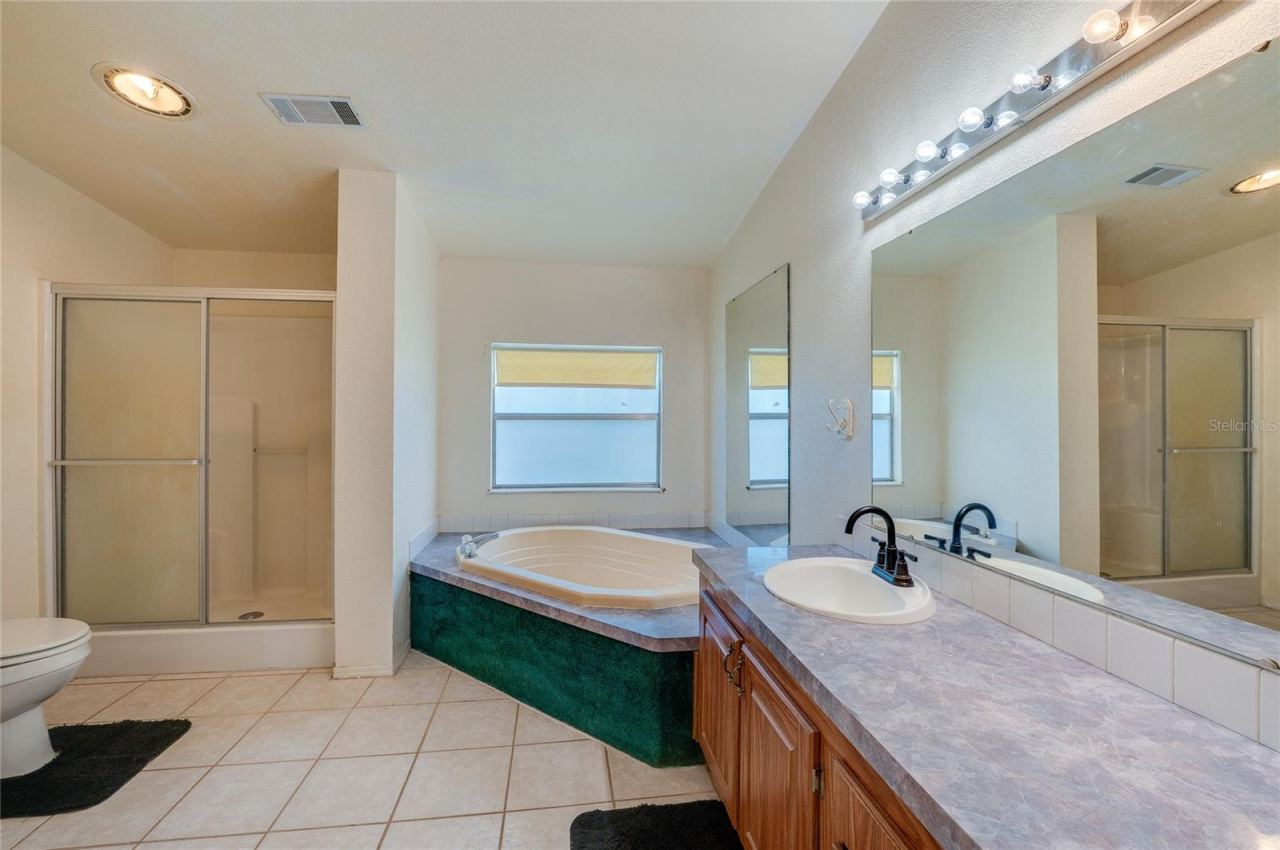 Photo 18 of 20: Large bathroom includes a corner soaking tub, separate enclosed shower, extended vanity with oversized mirror, and tile flooring.