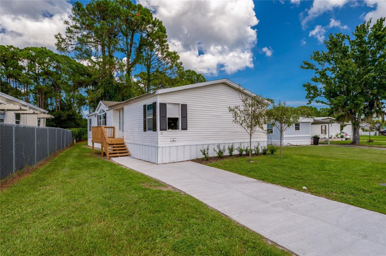 Photo 1 of 20: Front approach features a concrete walkway leading to a raised entry with wood steps, complemented by an open lawn and established landscaping.