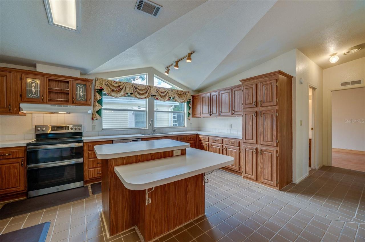 Photo 10 of 20: Another angle showcases the kitchen's generous cabinet storage, center island with multiple work surfaces, large windows, and vaulted architectural detail overhead.