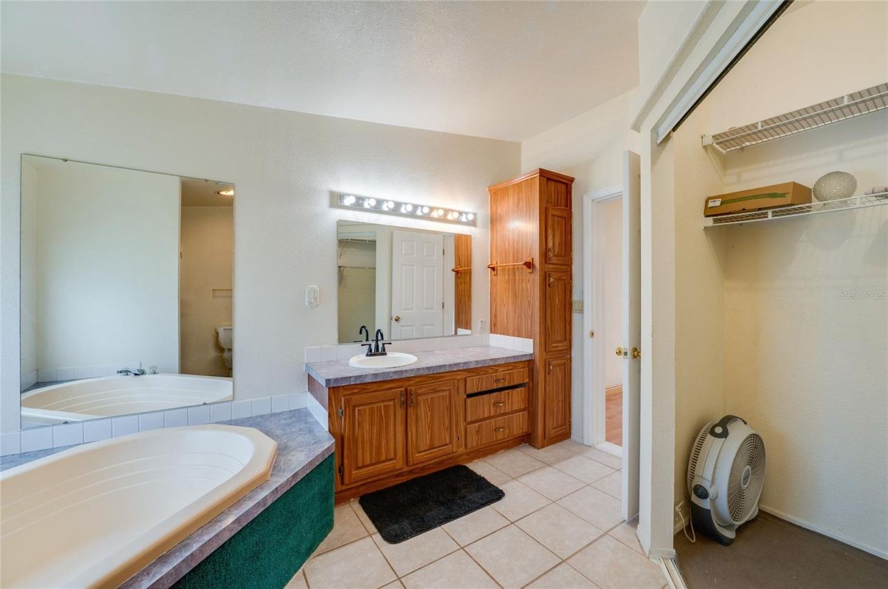 Photo 19 of 20: Additional view of the primary bath highlights the corner soaking tub, extended vanity, generous cabinetry, large mirrors, and adjacent closet storage.