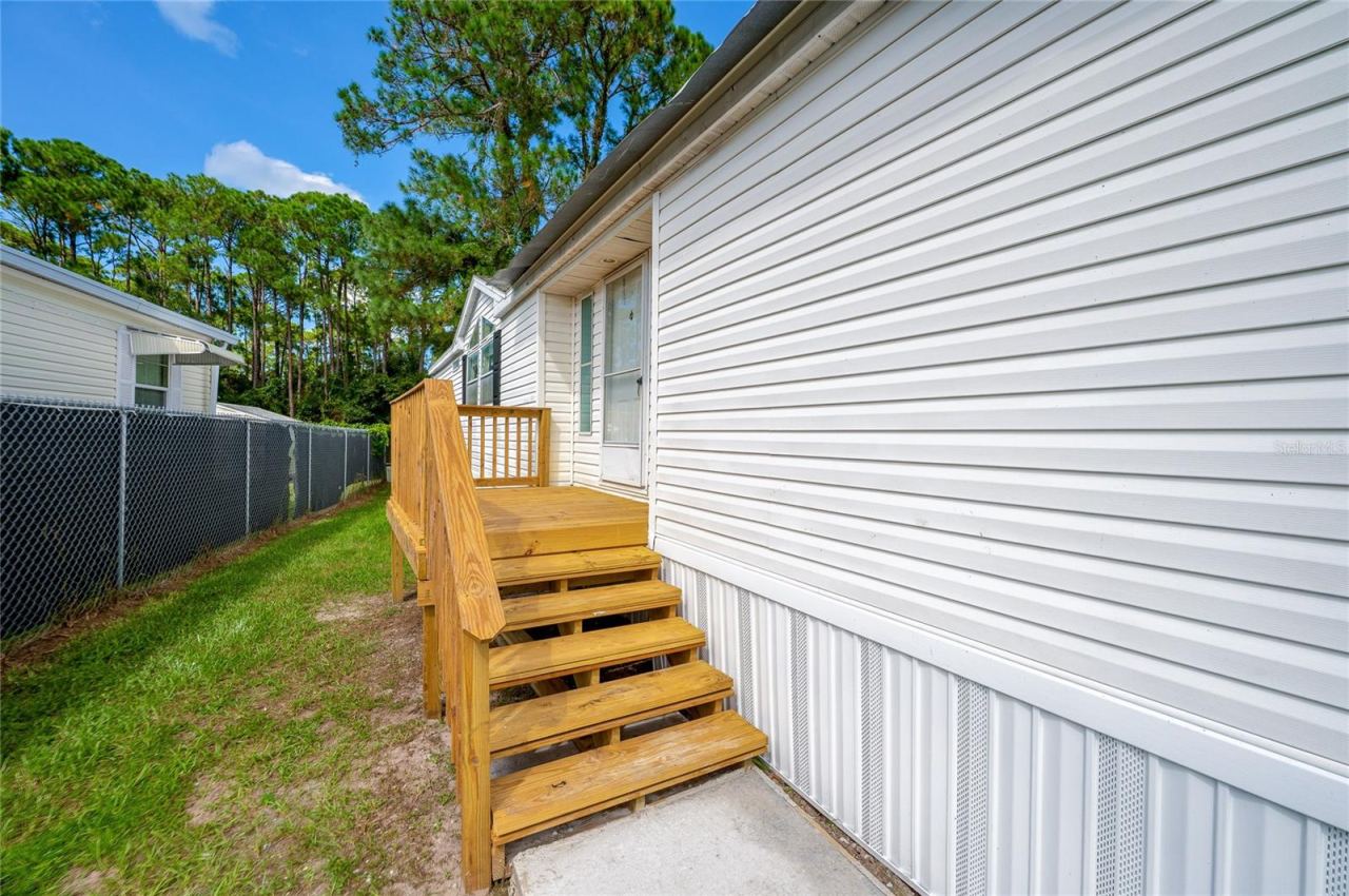Photo 3 of 20: Wood steps and a raised landing provide access to the home, with a grassy side yard alongside the residence.