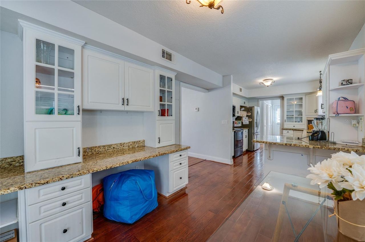Photo 16 of 20: Bright kitchen prep space featuring white cabinetry with glass-front uppers, granite countertops, and seamless laminate flooring leading to adjacent rooms.