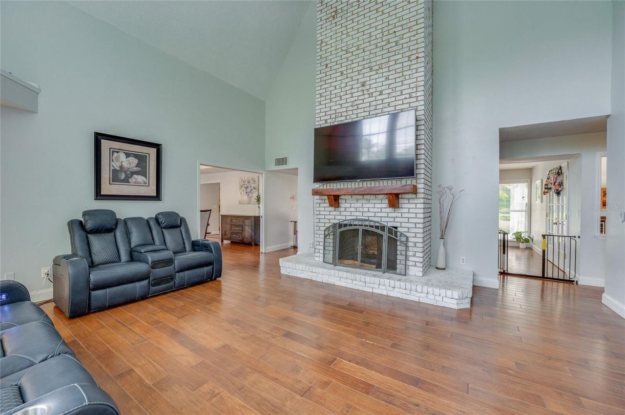 Photo 11 of 20: Soaring living room view centered around a floor-to-ceiling whitewashed brick fireplace with a rustic mantel and laminate flooring throughout.