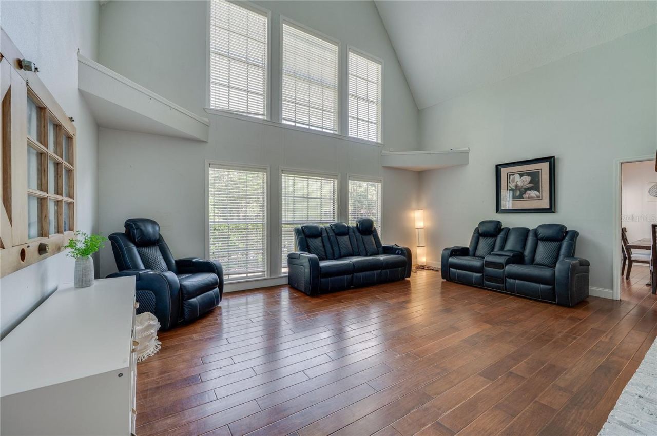 Photo 10 of 20: Grand living room highlighted by soaring vaulted ceilings, warm laminate floors, and a double-stacked bank of large windows offering abundant natural light.