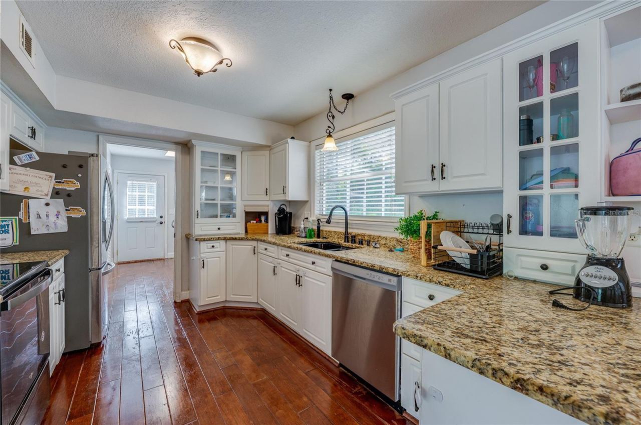 Photo 17 of 20: Bright, spacious kitchen showcasing white cabinetry, speckled granite countertops, stainless steel appliances, and rich laminate flooring.