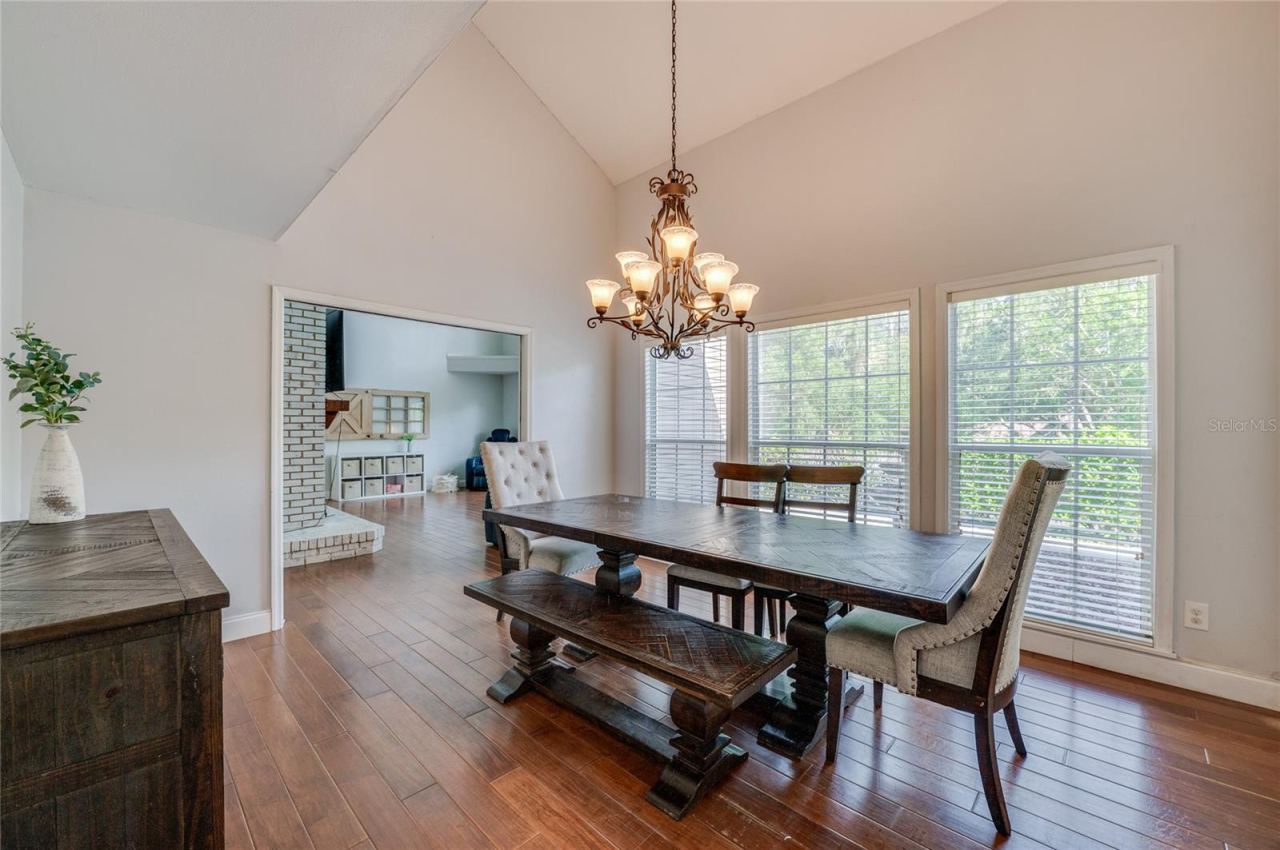 Photo 20 of 20: Open dining space featuring high ceilings, warm laminate floors, a classic chandelier, and a wide doorway connecting into the adjoining living room.