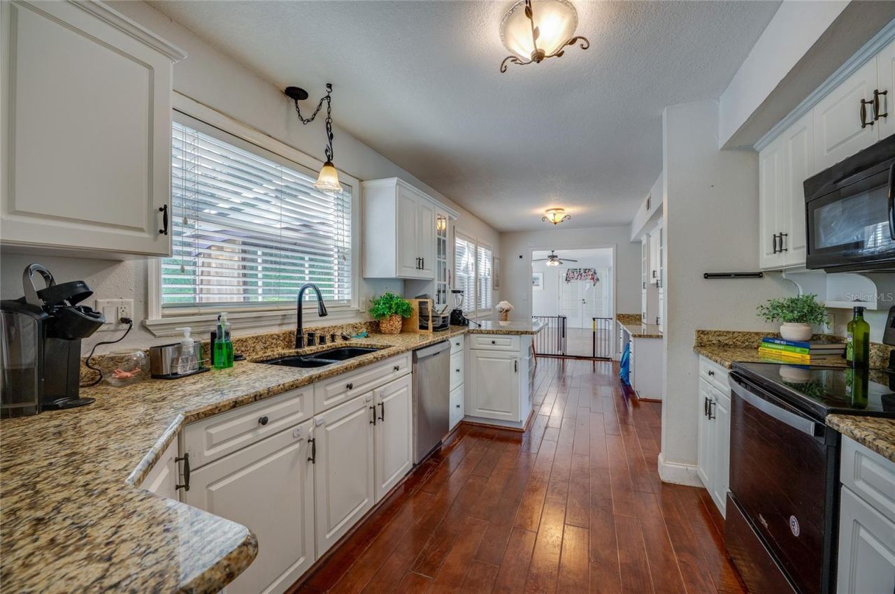 Photo 18 of 20: Long galley-style kitchen featuring granite countertops, crisp white cabinets, a black sink basin, and an open sightline through the home.