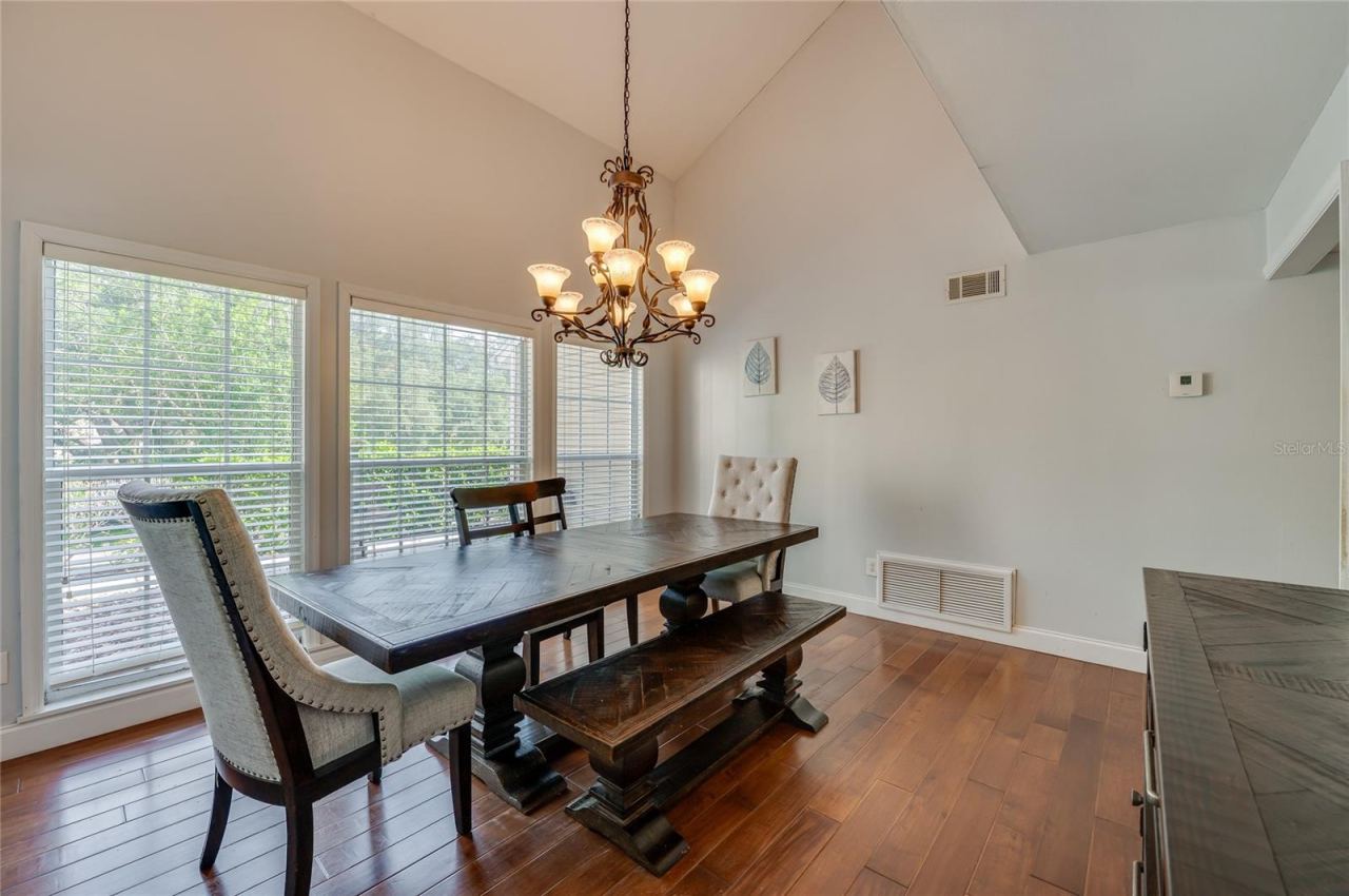 Photo 19 of 20: Formal dining area framed by vaulted ceilings and expansive windows, lit by an ornate iron chandelier over rich laminate floors.