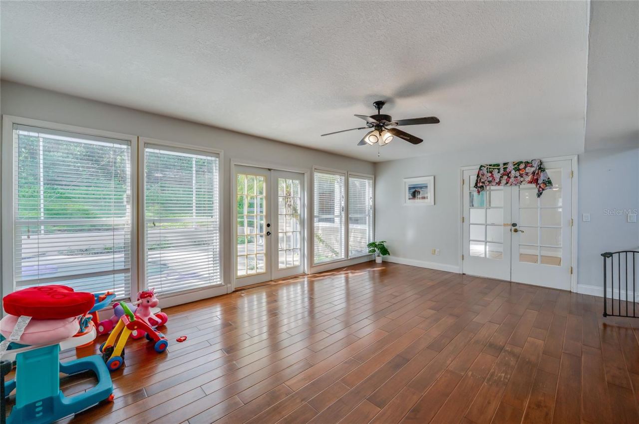 Photo 12 of 20: Open living area featuring rich laminate floors, a central ceiling fan, and multiple paned windows and glass doors opening to the outdoor pool patio.