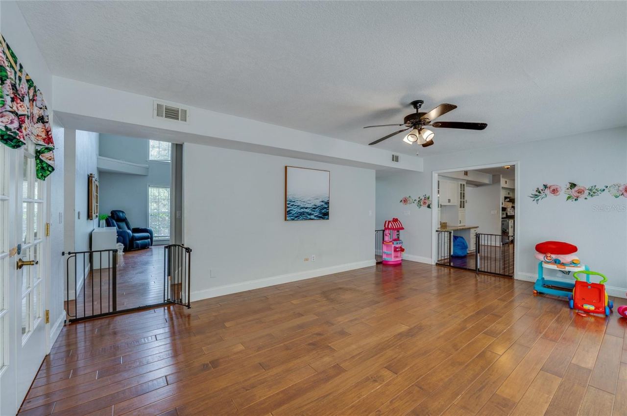 Photo 14 of 20: Versatile open room with rich laminate floors, a ceiling fan, and wide archway entrances connecting to surrounding living spaces.