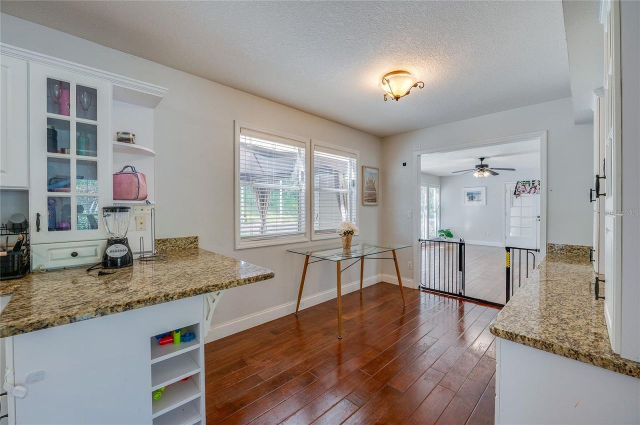 Photo 15 of 20: Functional kitchen nook featuring granite countertops, white cabinetry with display shelving, and rich laminate flooring.