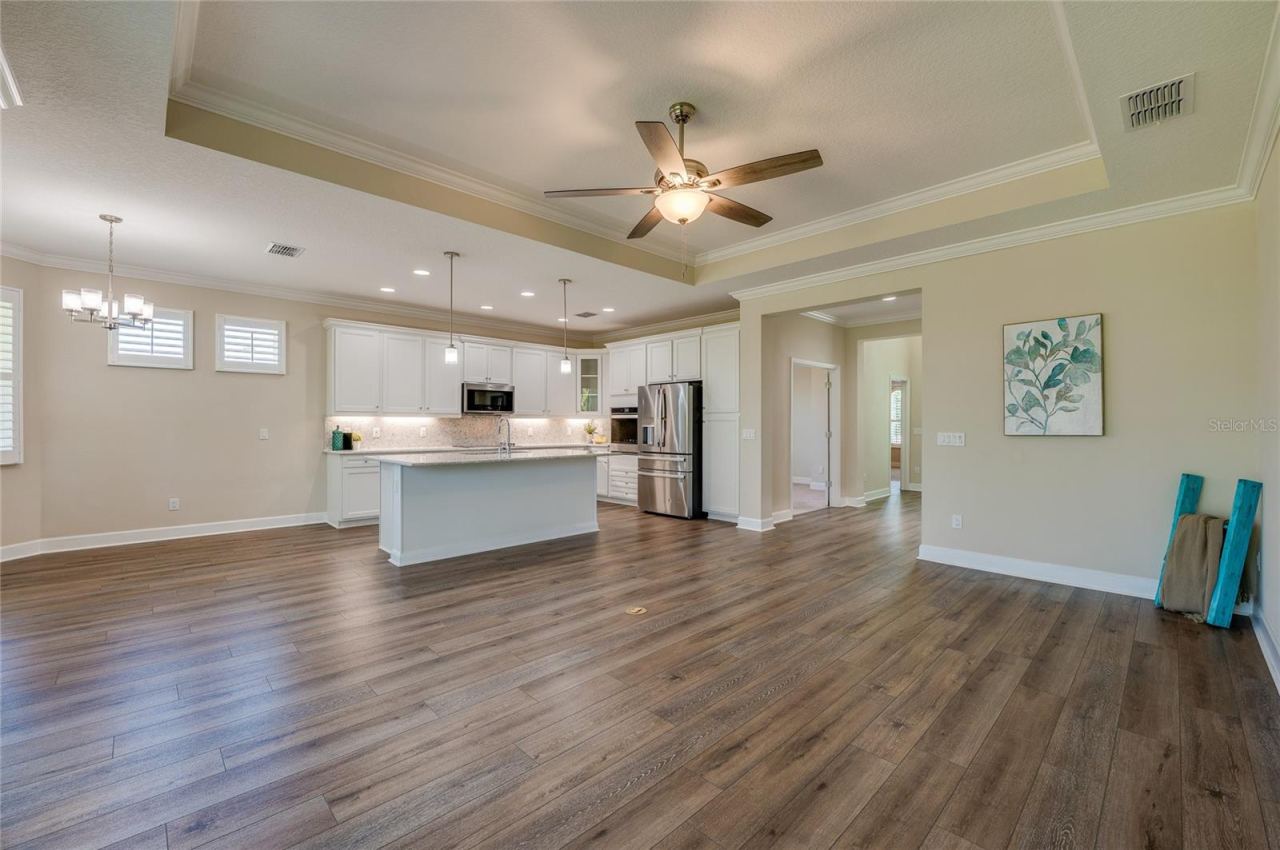 Photo 14 of 20: Expansive great room showing the seamless transition between the kitchen, dining nook, and living areas under a high tray ceiling.