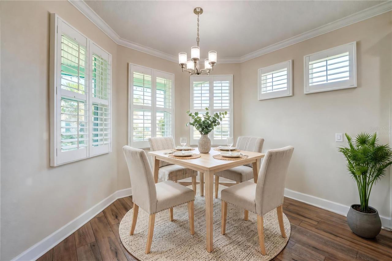 Photo 13 of 20: Virtually Staged - Sunlit dining nook featuring a bay window wall dressed in clean white plantation shutters and a classic multi-light chandelier overhead.