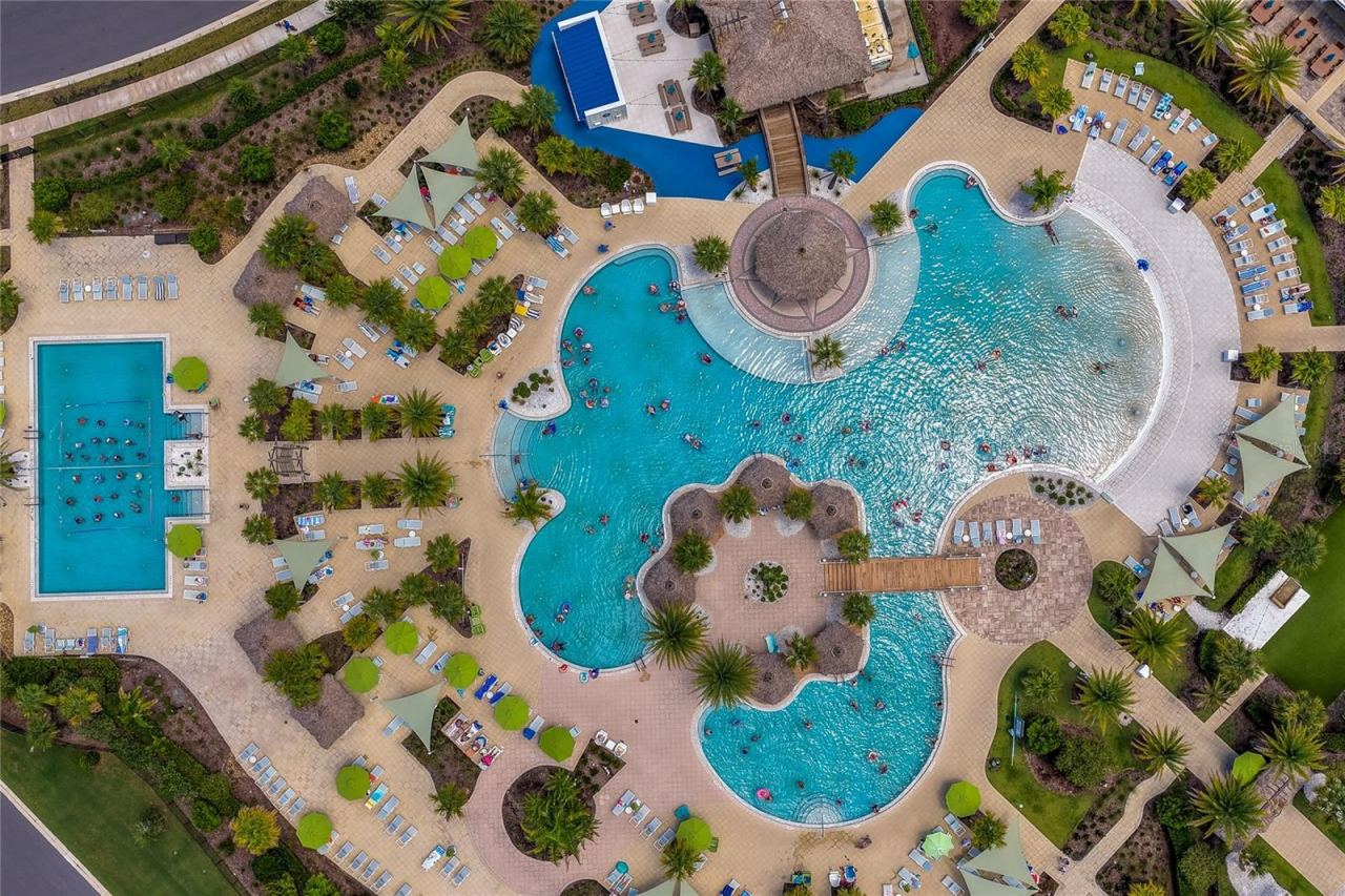 Photo 5 of 20: Dynamic top-down look at the massive resort-style pool area featuring a winding zero-entry swimming pool, dedicated lap lanes, and thatched-roof shade structures.