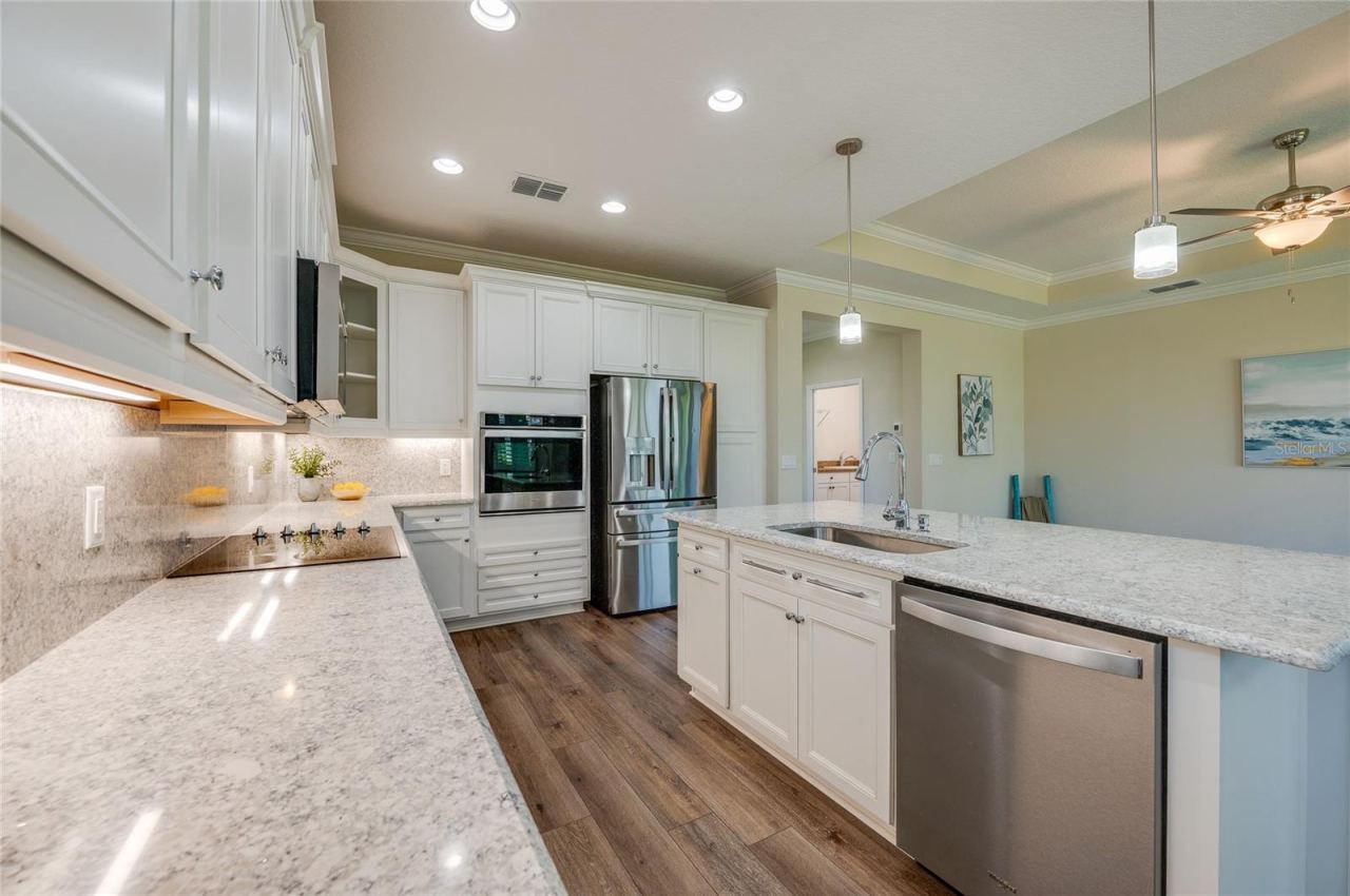 Photo 11 of 20: Long view of the kitchen work area highlighting expansive granite countertops, a built-in cooktop, and an integrated dishwasher in the island. Stylish glass pendant lights and recessed lighting illuminate the entire space.