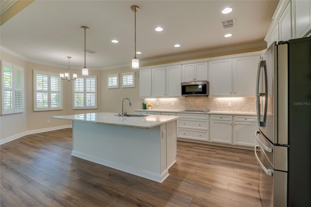 Photo 9 of 20: Spacious, open-concept kitchen featuring a large central island, granite countertops, white cabinetry, and stainless steel appliances.