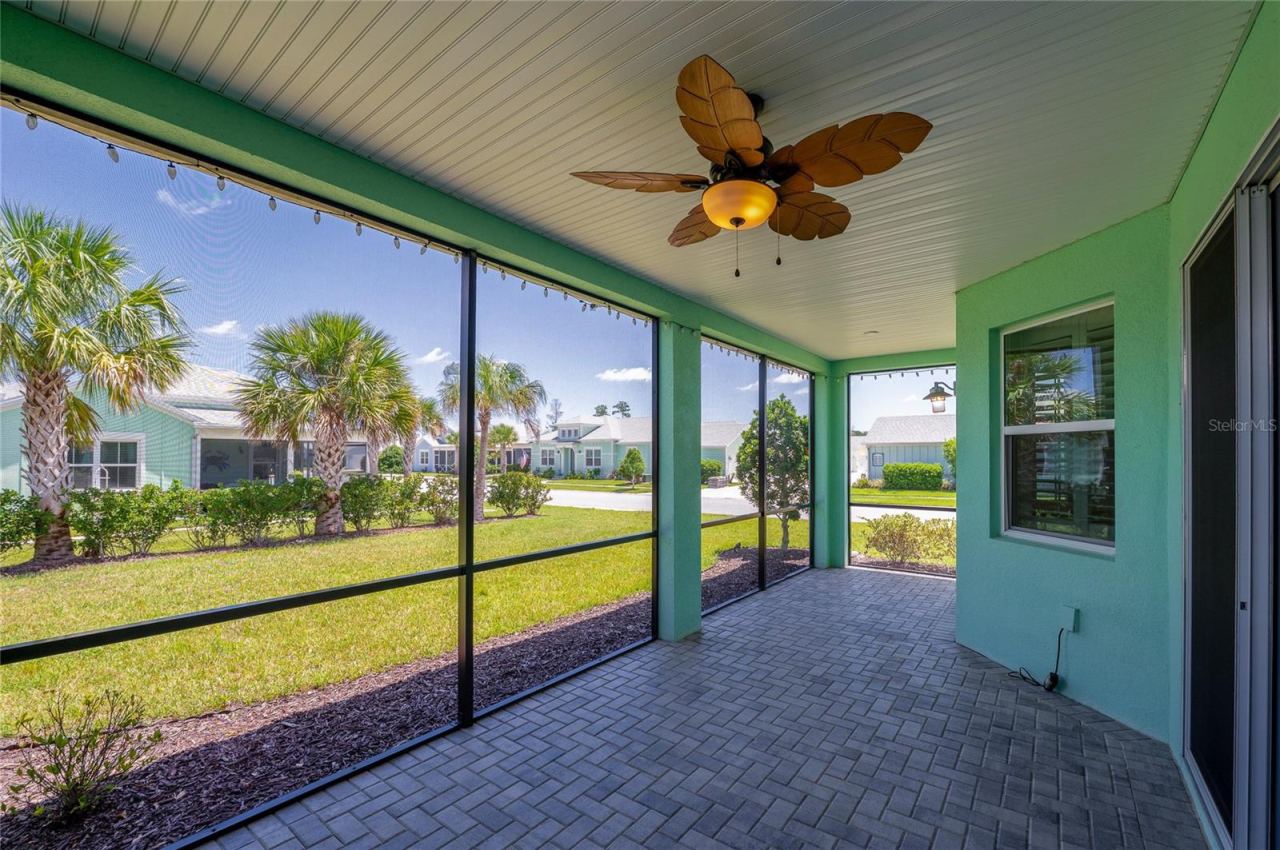 Photo 18 of 20: Alternate angle of the screened-in patio showcasing the mint-green stucco exterior, a large sliding glass door, and durable paver flooring.