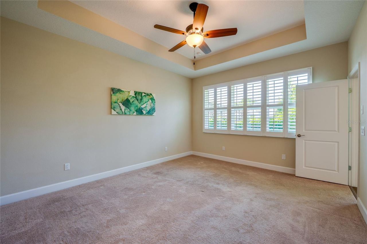 Photo 20 of 20: Reverse angle of the primary bedroom showcasing a large window wall fitted with white plantation shutters that fill the room with natural light.