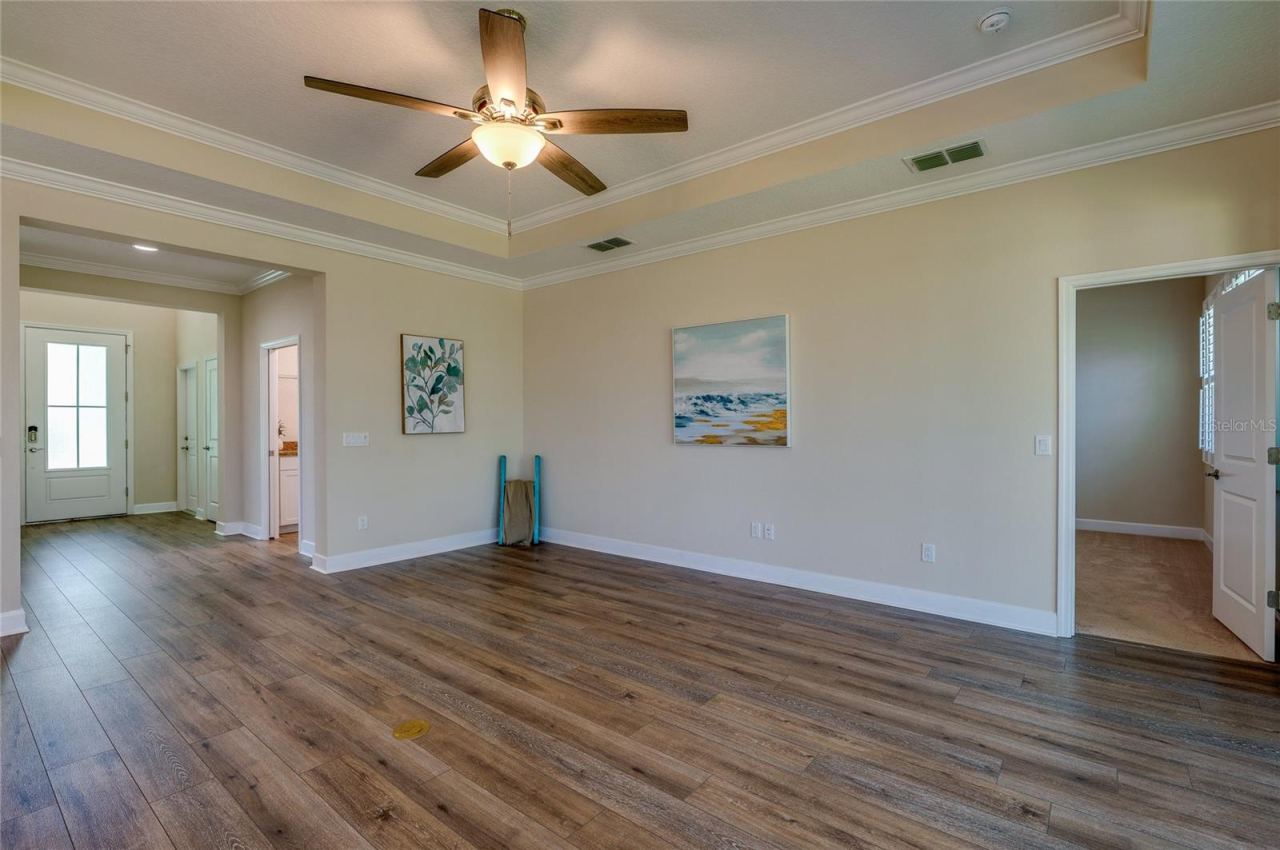Photo 16 of 20: Alternate view of the main living space looking toward the front foyer and an adjoining bedroom doorway. The continuous luxury vinyl flooring and tray ceiling enhance the room's open, cohesive design