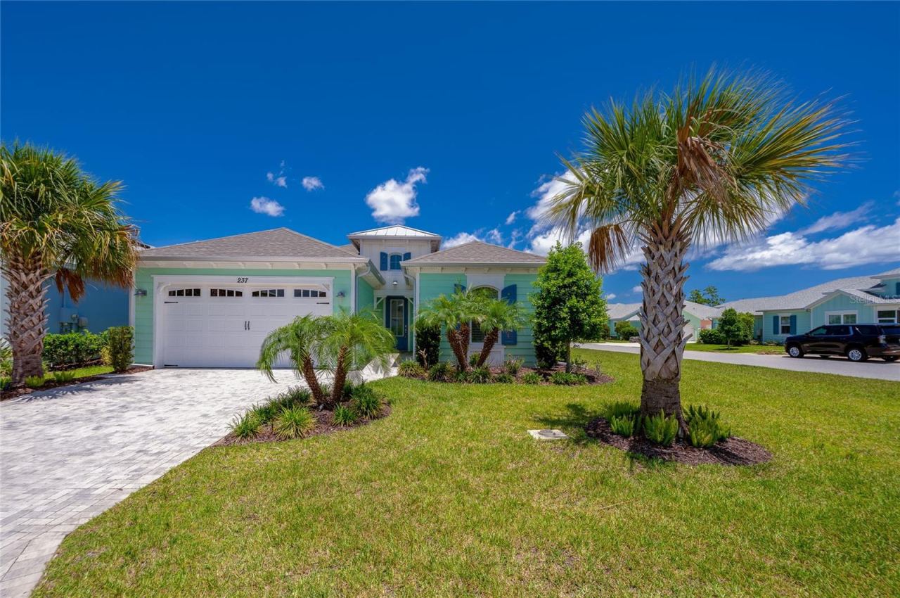 Photo 2 of 20: 4.Full front view of the coastal home showcasing its architectural design, paved driveway, entry tower, and tropical landscaping