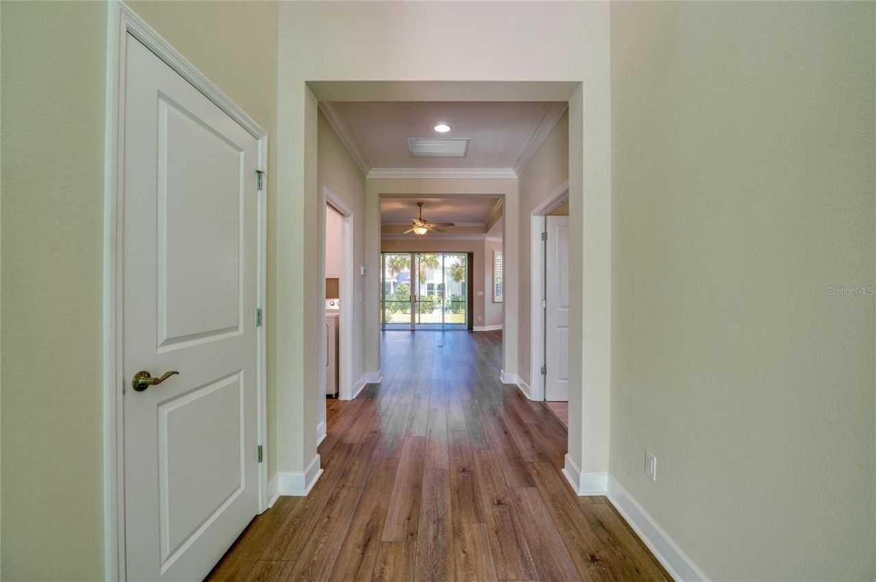 Photo 8 of 20: Bright entryway looking down a central hallway with wood-look flooring, leading toward a glass sliding door that opens to the screened in patio.