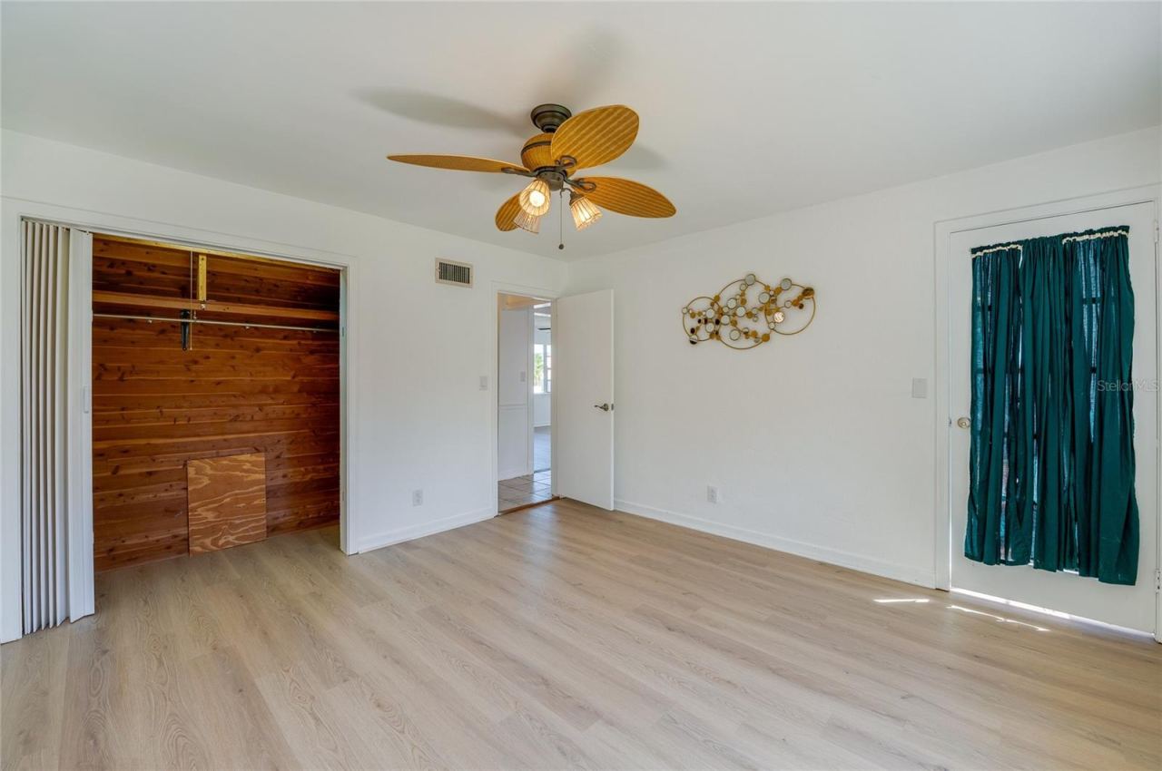 Photo 15 of 20: Versatile room displaying LVP flooring, a tropical-style ceiling fan, and a cedar-lined walk-in closet with built-in shelving. A glass-paneled exterior door with privacy drapery opens to an adjacent space.