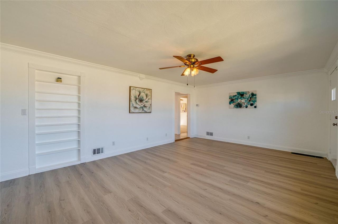 Photo 7 of 20: Open-concept living space framed by crisp white trim, continuous LVP flooring, and a built-in recessed wall shelving unit. The clean layout and central doorway provide an airy, connected atmosphere.