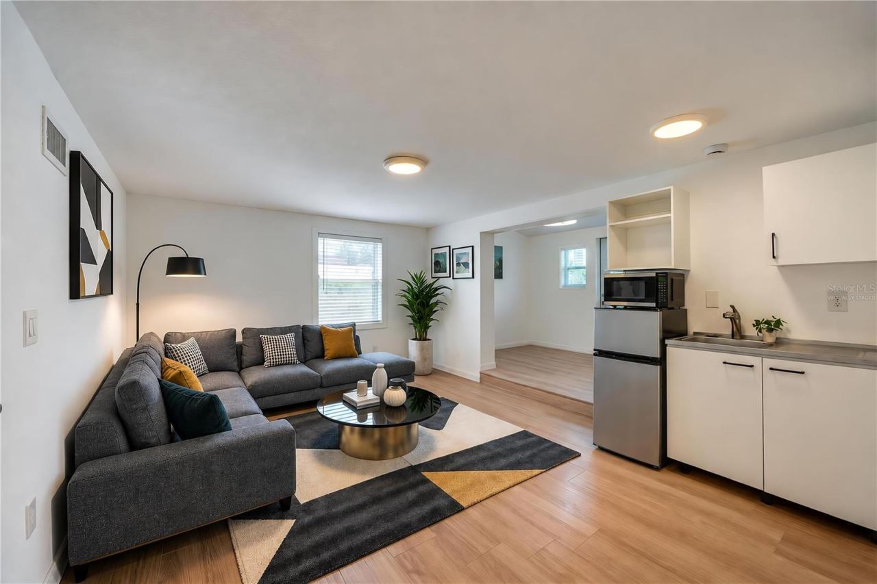 Photo 20 of 20: Virtually Staged - Open studio in law suite boasting modern kitchenette amenities including a compact refrigerator, microwave, sink, and low-profile cabinetry. Light LVP flooring and recessed overhead lights create a clean, contemporary feel.