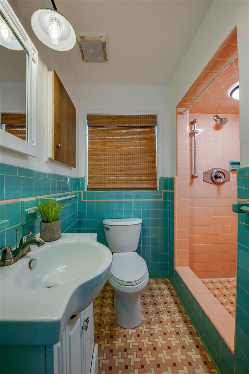 Photo 16 of 20: Vibrant vintage-style bathroom featuring turquoise wall tile, patterned geometric floor tile, and a matching pink-tiled walk-in shower stall. A white pedestal-style vanity with modern fixtures adds functional contrast.