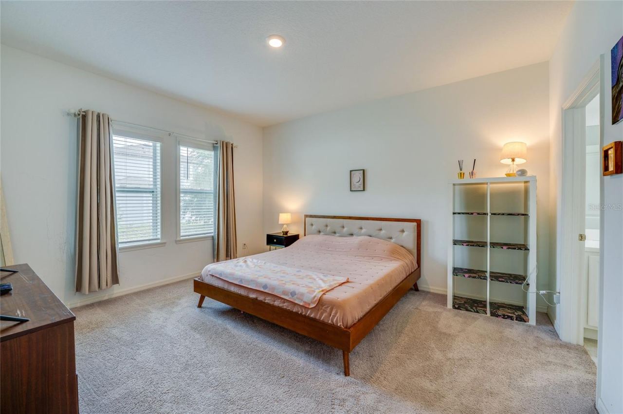 Photo 18 of 20: Bright and spacious primary bedroom featuring plush carpeting, soft neutral walls, and windows that invite ample natural light. An attached en-suite bathroom provides seamless convenience.