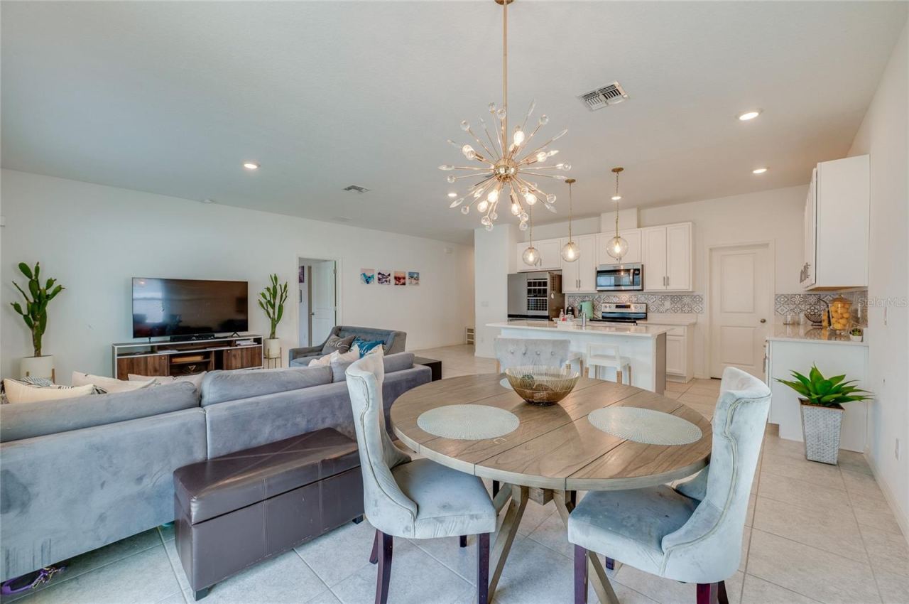Photo 17 of 20: An expansive look from the dining alcove back through the great room toward the kitchen, demonstrating a cohesive design tied together by matching light fixtures and uniform tile flooring.