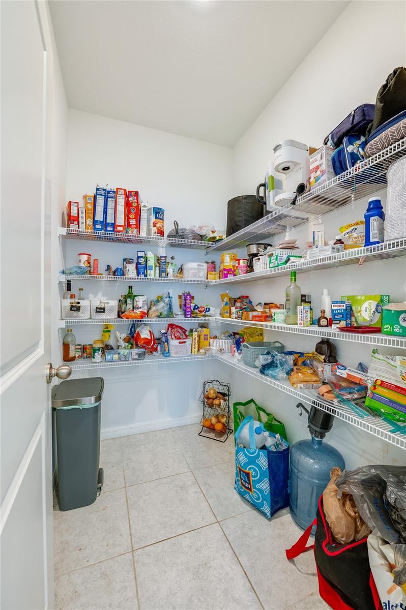 Photo 15 of 20: A deep, walk-in pantry equipped with multiple tiers of wire shelving wrapped around the walls for maximum storage efficiency. The space features tiled flooring and bright overhead lighting.