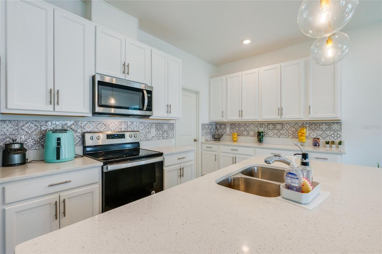 Photo 13 of 20: Detailed view of the kitchen's preparation area, highlighting the intricate gray and white patterned tile backsplash and under-cabinet clearance.