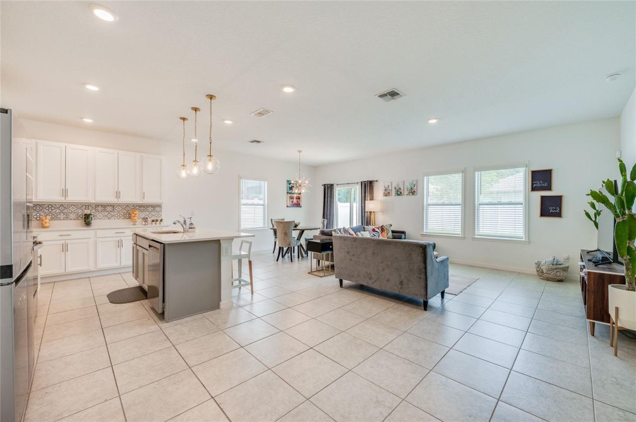 Photo 8 of 20: Bright, open-concept main living area showcasing durable tile flooring, recessed ceiling lights, and modern pendant light fixtures. The space seamlessly transitions from a contemporary kitchen with white cabinetry and an island into a spacious livin…